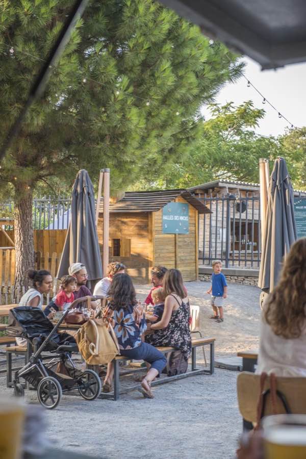 Terrasse extérieure des Halles du Verger sous les pins, tables et guirlandes